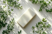Natural white soap bar surrounded by fresh green leaves and delicate shadow patterns on light background, minimalist eco-friendly skincare composition.
