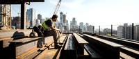 Construction worker in safety vest taking break on steel beams with urban skyline backdrop. Industrial development and city growth concept for business.