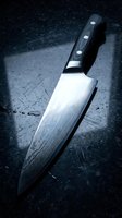 Professional chef knife with Damascus steel blade and black handle on dark granite surface for culinary cooking and food preparation.