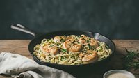 Pan-seared scallops with herb linguine pasta in cast iron skillet on rustic wooden table. Gourmet seafood dinner with fresh herbs and creamy sauce.