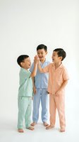 Three young Asian boys in colorful pajamas giving high five on white background. Happy children in sleepwear celebrating friendship and teamwork.
