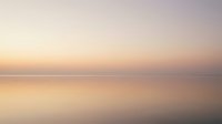 Serene seascape at dawn with calm waters reflecting soft pastel sky in warm golden and purple tones, suitable for backgrounds and wellness content.