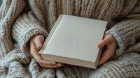 Hands holding open blank book with beige knit sweater, cozy reading moment for publishing, education, and lifestyle design projects.