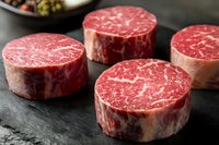 Raw marbled beef tenderloin steaks on black stone surface. Fresh premium cut filet mignon with white fat marbling pattern shows meat quality and texture.