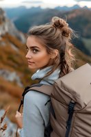 Young Caucasian woman with messy bun hairstyle wearing grey turtleneck sweater and carrying backpack while hiking in autumn mountains during sunset.