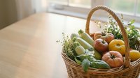 Wicker basket filled with fresh organic vegetables and fruits including tomatoes, cucumbers, and herbs on wooden table near window with natural daylight for farmers market, grocery, or healthy eating content.