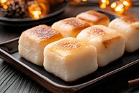 Fresh baked dinner rolls with golden brown tops served on dark plate with warm ambient lighting and bokeh background, close up view of soft bread texture.