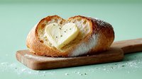 Fresh artisan bread roll with melted cheese heart shape on wooden cutting board, romantic breakfast concept for Valentine's Day celebration.
