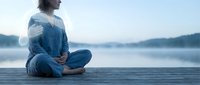 Young woman practicing meditation in lotus position on wooden dock by serene lake at dawn, peaceful mindfulness and wellness lifestyle concept.