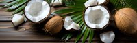 Fresh coconuts with green palm leaves on dark wooden background, whole and halved showing white flesh, tropical food ingredient for cooking.