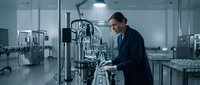 Professional female scientist in dark blue lab coat working with advanced laboratory equipment in modern sterile pharmaceutical manufacturing facility.