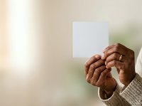 Mature adult with dark skin tone holding blank white card in hands against soft blurred background, suitable for messaging, advertising, and promotional campaigns.
