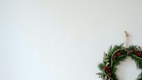 Festive evergreen wreath with red berries and twine bow hanging on white wall, perfect for holiday decorations and seasonal marketing materials.