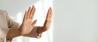 Male hands making stop gesture against white wall with natural lighting for rejection and refusal concepts.