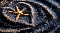 Golden starfish resting in heart-shaped sand formation on dark volcanic beach. Romantic ocean love symbol for wedding invitations, Valentine's Day cards, coastal decor.