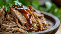 Tender slow-cooked pulled pork with glossy barbecue sauce in rustic wooden bowl, garnished with fresh herbs for comfort food and restaurant menu concepts.