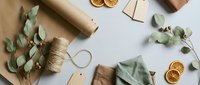Eco-friendly gift wrapping supplies with kraft paper, twine, eucalyptus leaves and dried orange slices arranged on white background for sustainable packaging.