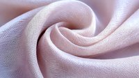 Soft pink linen fabric with elegant swirl pattern showcasing natural textile texture and flowing drape for fashion design and home decor projects.