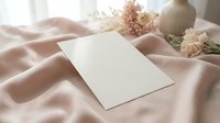 Blank white card mockup on soft pink silk fabric with dried flowers and ceramic vase in natural sunlight for wedding invitations and stationery design.