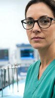 Professional female dentist with glasses in green scrubs at modern dental clinic office ready for patient care and oral health treatment.