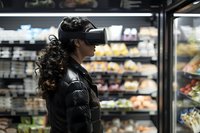 Woman wearing virtual reality headset shopping in grocery store with refrigerated display cases in background.