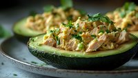 Stuffed avocado halves filled with creamy chicken salad and fresh herbs on rustic plate. Healthy low-carb meal option for lunch or dinner preparation.