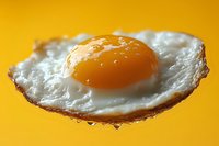 Sunny side up fried egg with crispy edges and bright orange yolk on vibrant yellow background, macro food photography showing texture and details for culinary use.