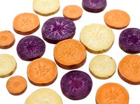 Colorful sliced carrots in purple, orange, and yellow varieties scattered on white background, showcasing natural diversity for food and nutrition concepts.