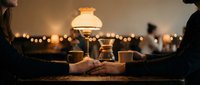 Romantic dinner date with couple holding hands across table illuminated by vintage oil lamp creating intimate atmosphere with warm bokeh lights.