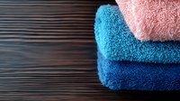 Stack of folded soft cotton towels in pink and blue shades on dark wooden background, creating cozy bathroom or spa atmosphere with gentle color contrast.