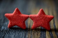 Two red fabric stars with textured surface sitting on dark striped material, suitable for rating, feedback, quality assessment, customer satisfaction, and review concepts.