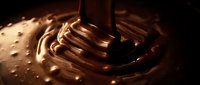 Liquid chocolate pouring and swirling with glossy texture, creating rich brown waves and splashes for food, beverage, and confectionery design projects.