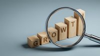 Wooden blocks spelling GROWTH under magnifying glass on gray background representing business development and progress analysis concept.