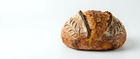 Freshly baked artisan sourdough bread loaf with golden crust and decorative scoring on clean white background for bakery and food photography.