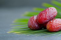 Fresh dates fruit on palm leaf background for healthy eating and Middle Eastern cuisine preparation.