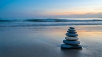 Zen stone stack on peaceful beach at sunset with gentle waves and colorful sky reflection on wet sand creating tranquil meditation atmosphere.