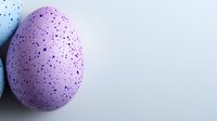 Speckled purple Easter egg on light background with dark spots and natural texture, minimalist holiday composition for seasonal designs and celebrations.