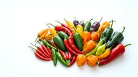 Assorted fresh chili peppers in red, yellow, orange and green varieties arranged on white background for culinary and cooking projects.