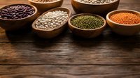 Assorted legumes and pulses in wooden bowls on rustic table. Black beans, white beans, green lentils, red lentils displayed for cooking, nutrition, and food styling projects.