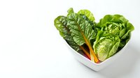 Fresh green leafy vegetables arranged in heart-shaped white bowl, featuring vibrant romaine lettuce with colorful stems. Suitable for healthy eating, nutrition, wellness, and diet-related content.