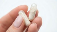 Hand holding two white capsules pills medication supplements on clean background for healthcare pharmaceutical design.