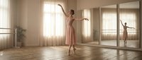 Young Caucasian woman ballet dancer practicing graceful movements in bright studio with wooden floors and large mirrors reflecting natural sunlight.
