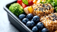 Fresh healthy meal prep container with sesame crusted chicken, steamed broccoli, colorful bell peppers and ripe blueberries for balanced nutrition and portion control.
