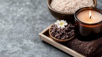 Spa wellness composition with aromatic salt, burning candle and brown towel on concrete background. Relaxation and body care concept.