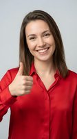 Smiling young Caucasian businesswoman in red shirt showing thumbs up gesture against gray background for corporate marketing and success concepts.