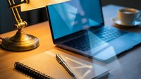 Cozy home office desk with laptop, notebook, pen, and coffee cup under warm lamp light, creating a productive workspace atmosphere.