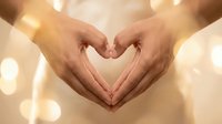 Two hands forming a heart shape against a warm golden bokeh background, symbolizing love, care, and connection for Valentine's Day or wellness concepts.