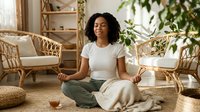 Young woman of African descent meditating in serene living room with rattan furniture, potted plants, and natural light for wellness and mindfulness content.