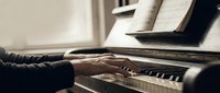 Close-up of hands playing piano with sheet music, warm lighting creates intimate atmosphere for music education and practice sessions.