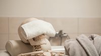 Rolled white towel and natural spa essentials arranged on neutral bathroom counter with blurred faucet background for wellness and relaxation themes.